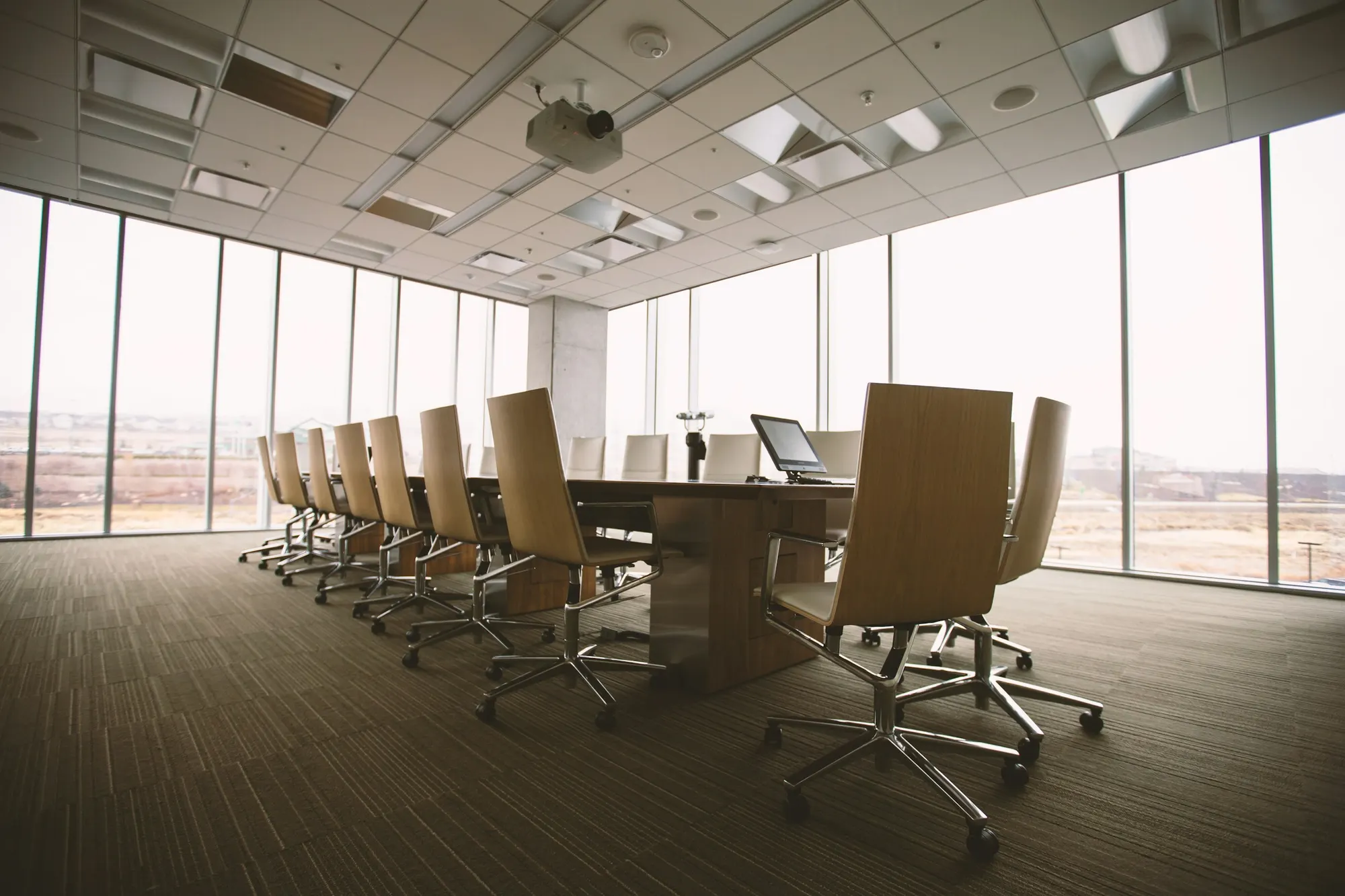 An empty boardroom with a long table, leather chairs, and floor-to-ceiling windows
