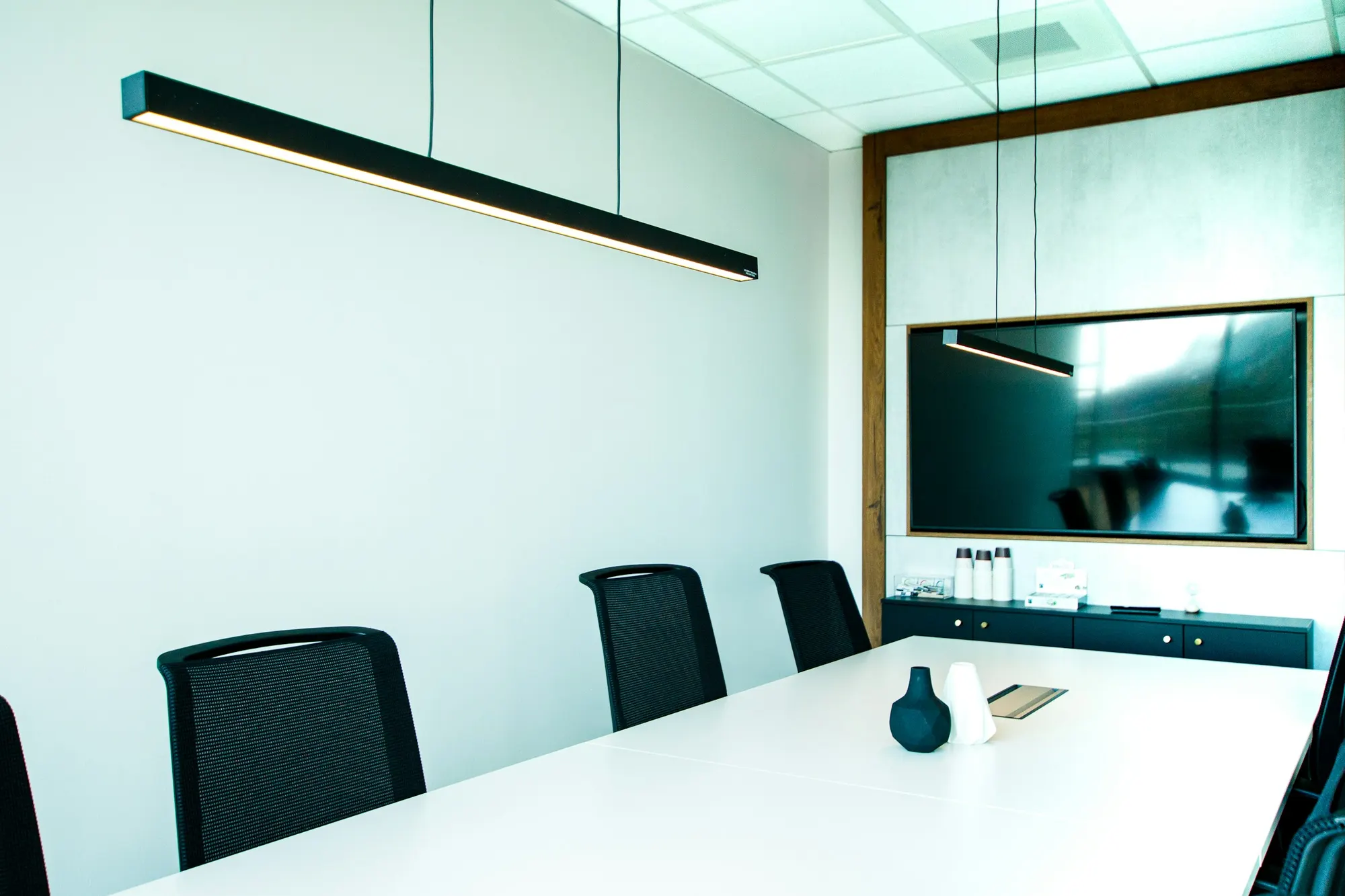 A minimal conference room with a white table, black mesh chairs, and a wall display